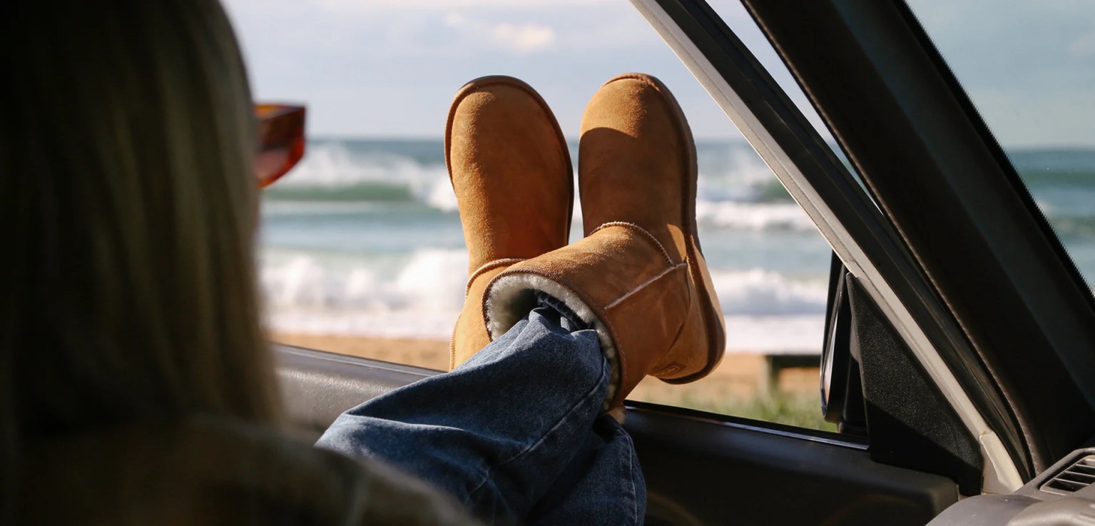 A woman wearing Ugg boots sits in a car with her feet out of the window, illustrating expert warnings that loose‑fitting footwear can put drivers at risk of fines.