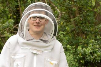 Young Welsh beekeeper Dafydd Pett wearing a white hooded beekeeping outfit, standing beside his hives. Finalist in the BBC Countryfile Young Countryside Champion Award 2025.