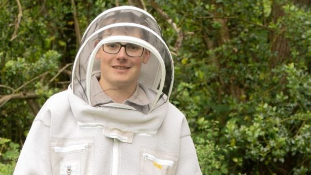Young Welsh beekeeper Dafydd Pett wearing a white hooded beekeeping outfit, standing beside his hives. Finalist in the BBC Countryfile Young Countryside Champion Award 2025.