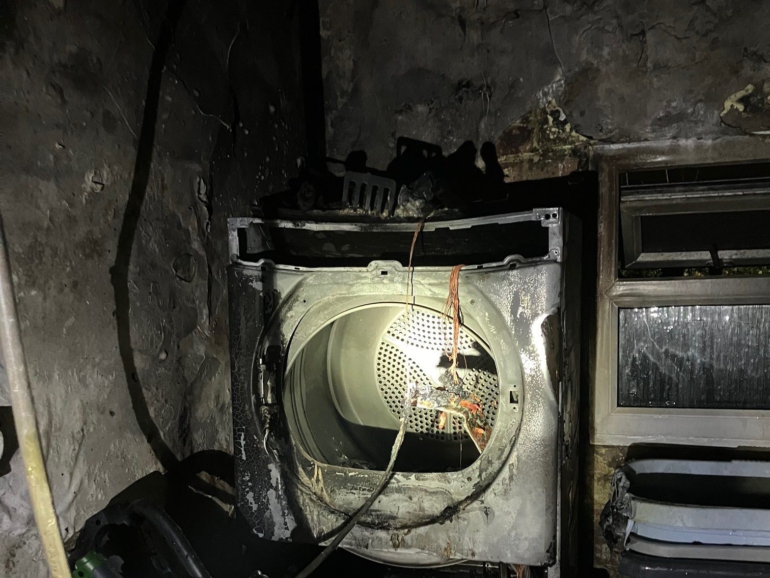 Burnt tumble dryer inside blackened outbuilding following fire in Penlan, Swansea.