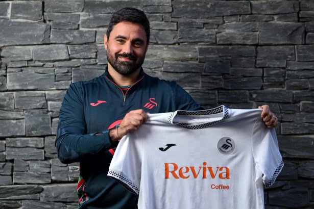Vítor Matos stands in front of a stone wall holding a white Swansea City AFC jersey featuring the Joma logo and Reviva Coffee sponsor, wearing a navy club jacket with red accents.