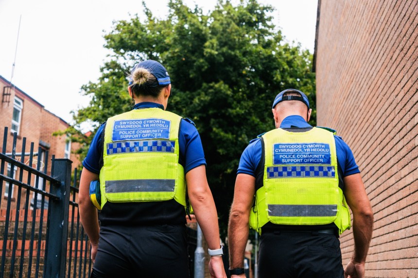 Two PCSOs in high-visibility vests walking through Bridgend town centre during a dispersal order enforcement period.