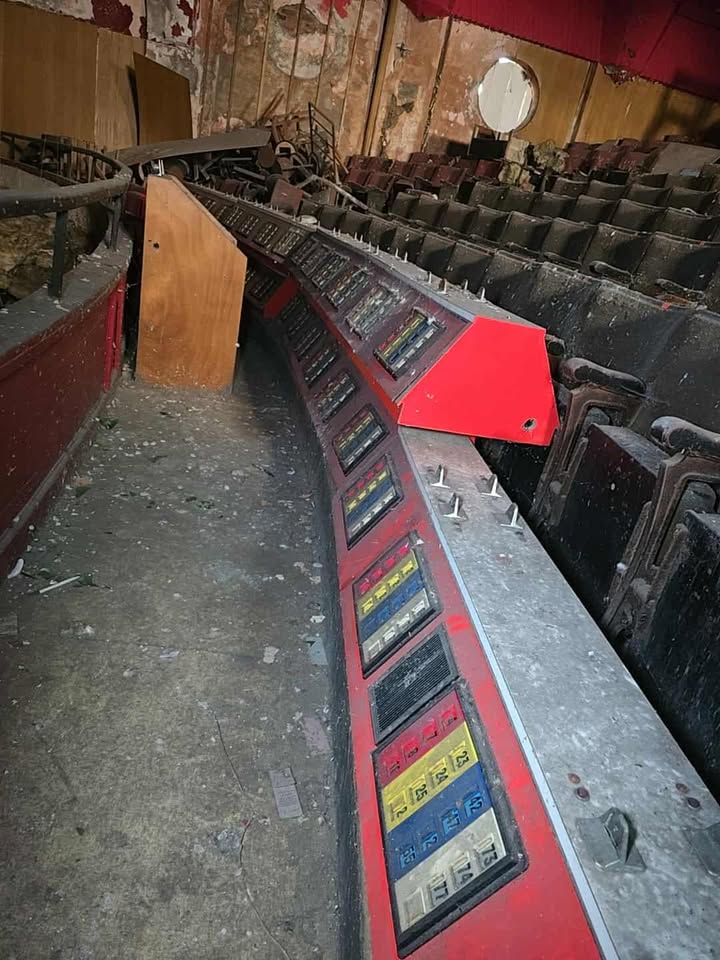 Abandoned control panel with coloured buttons in deteriorated auditorium with dusty seating and peeling walls.