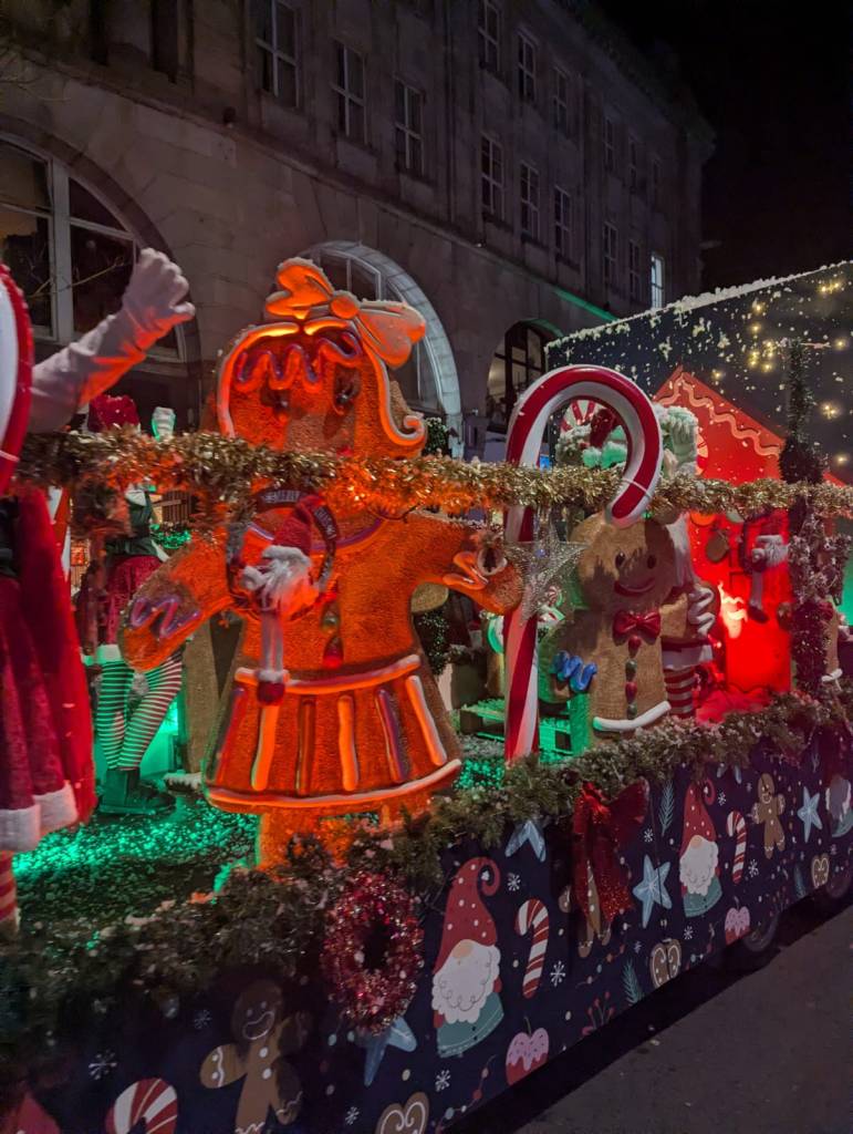 Parade float with gingerbread girl, candy canes, and holiday decorations.