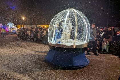 Illuminated snow globe with castle and snow-covered trees, surrounded by spectators.