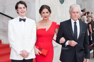 Catherine Zeta‑Jones in a red dress on the red carpet outside Brangwyn Hall, with Michael Douglas and their son Dylan, attending her Freedom of the City ceremony in Swansea.