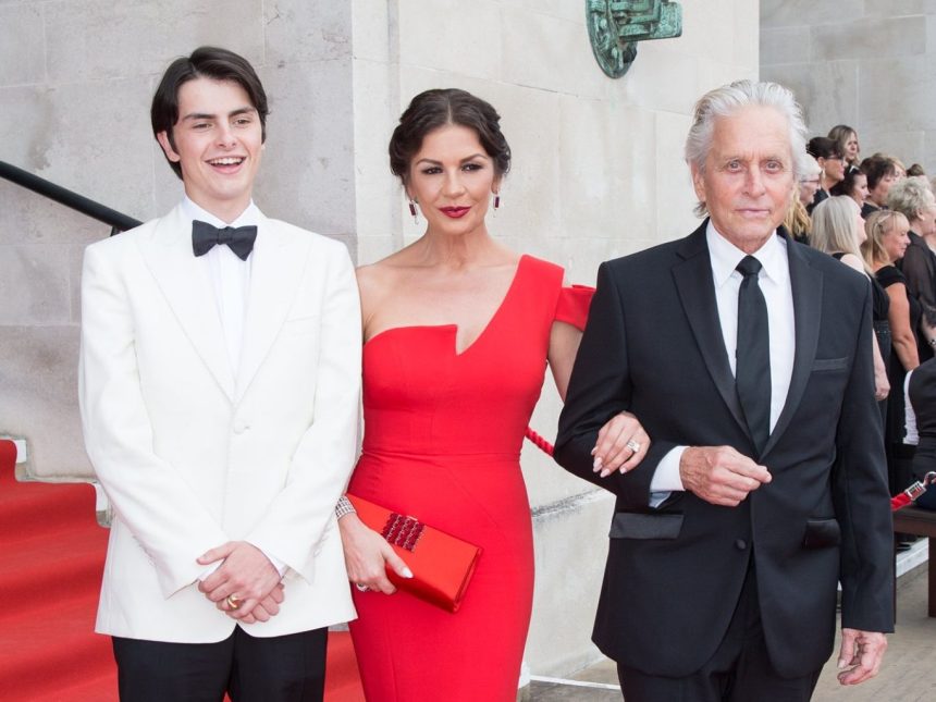 Catherine Zeta‑Jones in a red dress on the red carpet outside Brangwyn Hall, with Michael Douglas and their son Dylan, attending her Freedom of the City ceremony in Swansea.