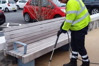 Council worker using specialist cleaning equipment on Mumbles Prom to remove stains beneath new benches.