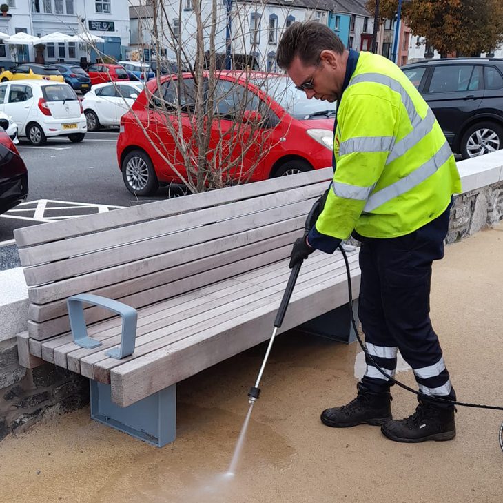 Council worker using specialist cleaning equipment on Mumbles Prom to remove stains beneath new benches.