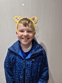 Dewi, a 10‑year‑old boy from Swansea, smiling in Pudsey Bear ears before his BBC Children in Need Choir performance.