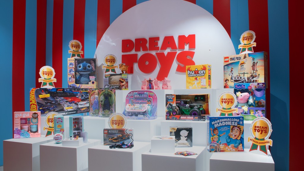 Display of children’s toys featured in the DreamToys 2025 list, including LEGO, Peppa Pig, Hot Wheels, and Stitch, arranged on white platforms with red festive backdrop.