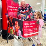 Grandad and young granddaughter standing at a Tesco donation point in Swansea, handing over toys for the Mr X Christmas Appeal.