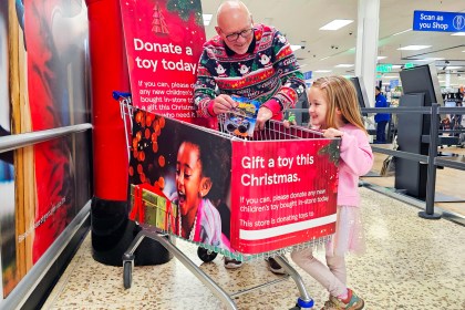 Grandad and young granddaughter standing at a Tesco donation point in Swansea, handing over toys for the Mr X Christmas Appeal.