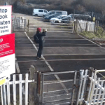 Person standing on railway tracks at Port Talbot crossing photographing approaching train.
