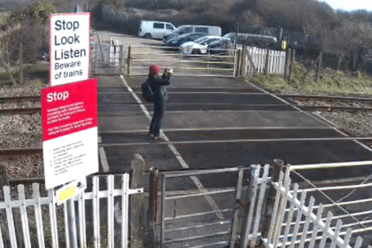 Person standing on railway tracks at Port Talbot crossing photographing approaching train.