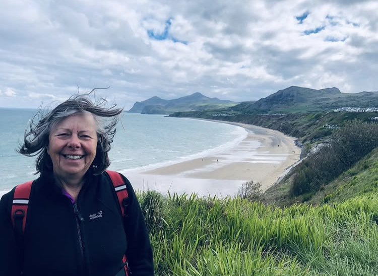 Janet Baldock standing on a cliffside overlooking a beach during her Wales Coast Path walk