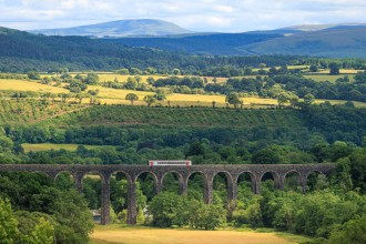 A single train crosses a stone viaduct over a green valley on the Heart of Wales line.