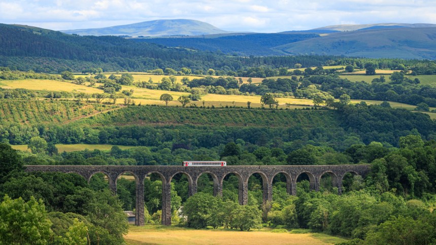 A single train crosses a stone viaduct over a green valley on the Heart of Wales line.
