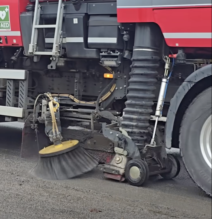Side closeup of road sweeper lorry showing brushes working at Cwmbwrla roundabout.