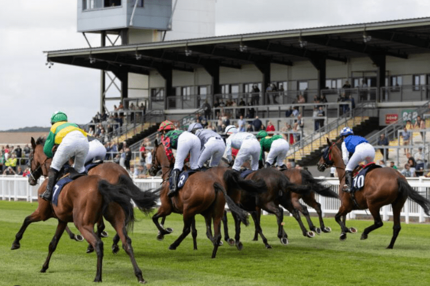Horses and jockeys racing over hurdles at Ffos Las Racecourse in Carmarthenshire, Wales.