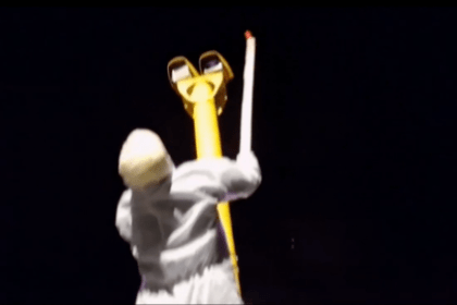 Still image from video showing a hooded man in a white boiler suit painting red paint over a Swansea speed camera lens with a brush on a stick.