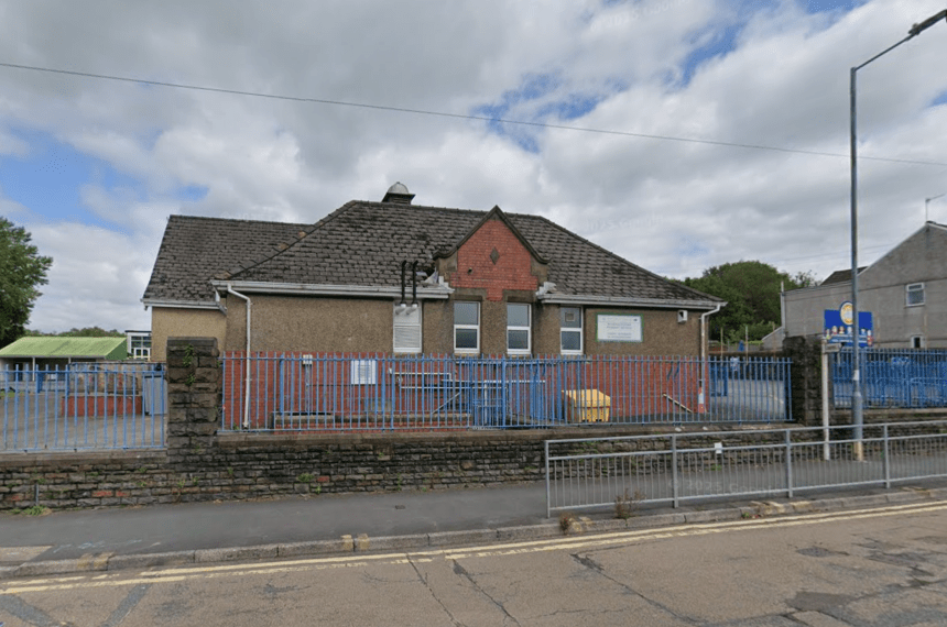 Single-storey school building with pitched roof, blue fencing, and stone wall, located in Bryncoch, Neath.