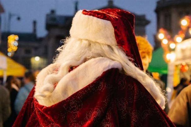 Traditional Santa walking through festive Christmas market with lights and stalls in Swansea.