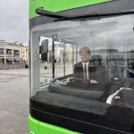 Tom Giffard MS sitting in the driver’s seat of a green electric double‑decker bus.