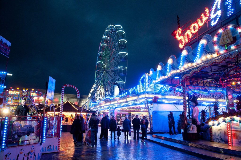 Ferris wheel and carousel at Swansea’s Winter Wonderland, with colourful lights and crowds