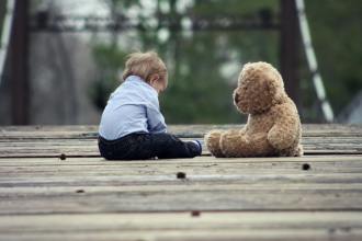 boy sitting with brown bear plush toy on selective focus photo