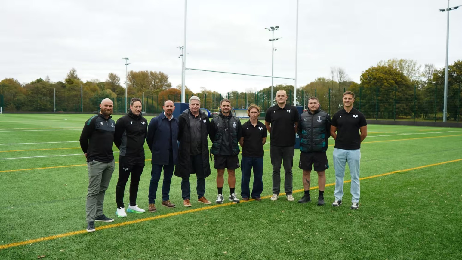 Ten individuals from Ospreys and Swansea University standing on a rugby pitch at St Helen’s, marking the launch of their new elite rugby development partnership.