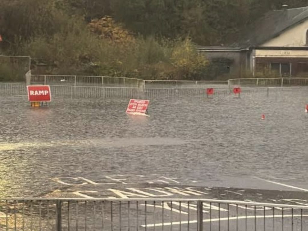 Floodwater covers Cwmbwrla roundabout in Swansea, with road closed signs standing in deep water.
