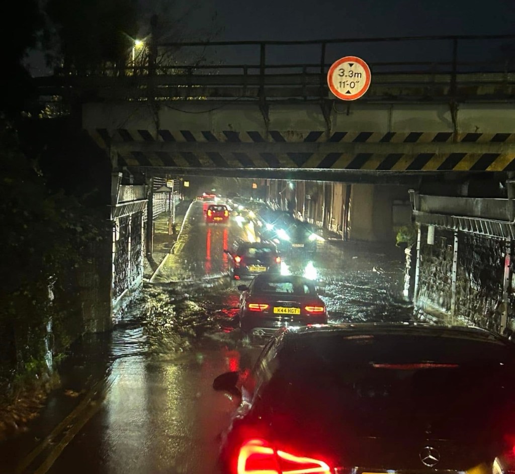 Vehicles drive slowly through floodwater beneath the railway bridge on Mill Street, Gowerton.