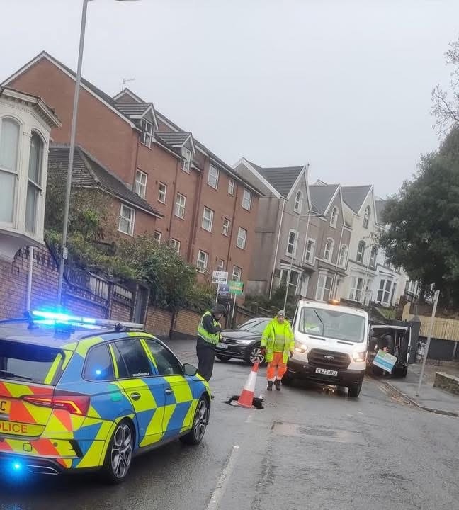 Police and utility workers at the scene of a sinkhole on Bryn-y-Mor Road, Swansea, with traffic cones and vehicles blocking the road.