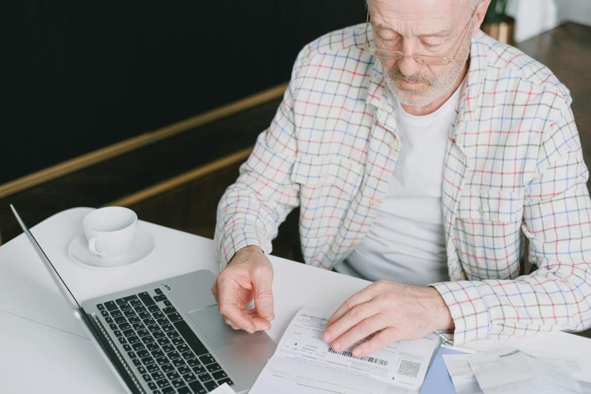 an elderly man looking at the documents on the table near his laptop