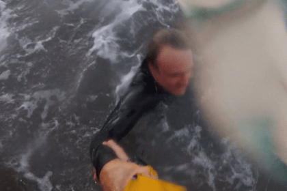 Surfer grabbing RNLI rescuer’s hand during lifeboat rescue off Rest Bay.