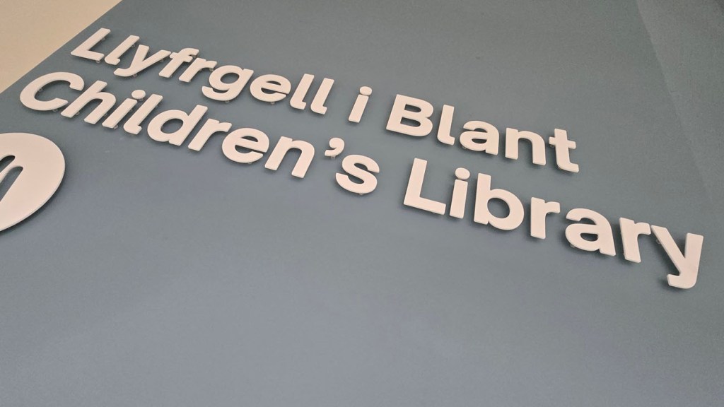 Wall sign reading “Llyfrgell i Blant / Children’s Library” at Y Storfa in Swansea.