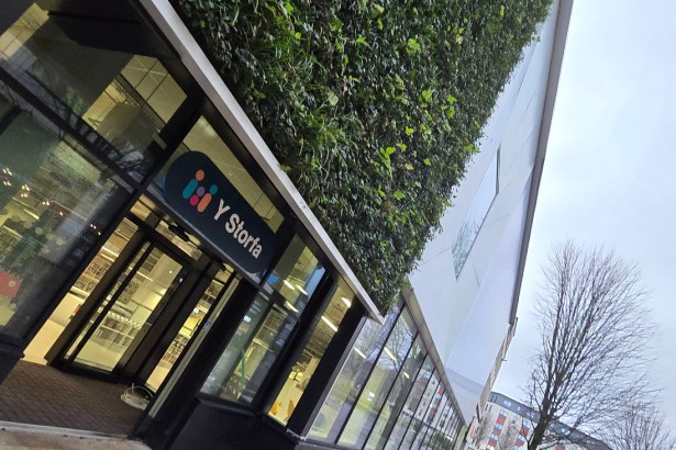 Glass entrance to Y Storfa with green wall and logo above the doors.