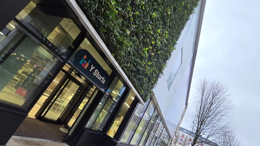 Glass entrance to Y Storfa with green wall and logo above the doors.
