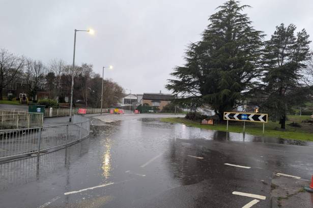Flooded road surface near Cwmbwrla Roundabout with traffic signs and barriers visible.