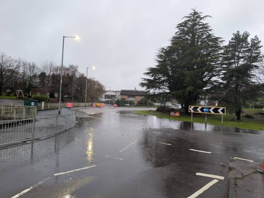 Flooded road surface near Cwmbwrla Roundabout with traffic signs and barriers visible.