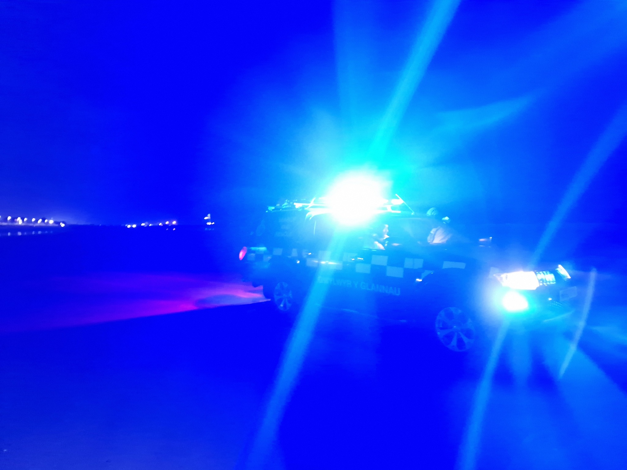 A Coastguard rescue vehicle lighting up the shoreline at night at Aberavon Beach