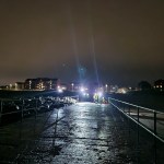Emergency crews in high‑visibility gear respond to a nighttime rescue on the North Pier at Aberavon Beach, with bright floodlights reflecting off the wet surface.