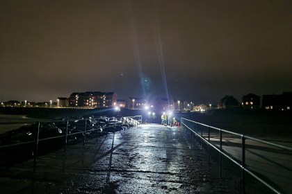 Emergency crews in high‑visibility gear respond to a nighttime rescue on the North Pier at Aberavon Beach, with bright floodlights reflecting off the wet surface.