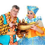 Joe Pasquale and Kev Johns in colourful pantomime costumes holding a genie lamp, promoting Aladdin at Swansea Grand Theatre. Credit: Swansea Grand / Imagine Theatre