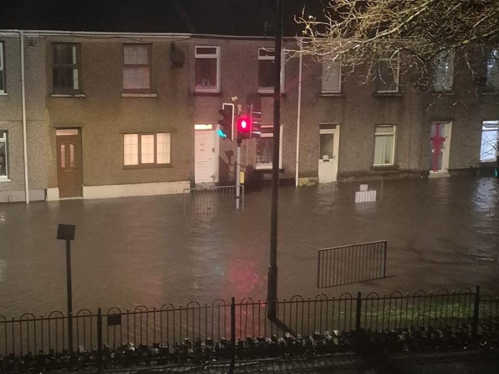 Nighttime flooded residential street in Briton Ferry, water reaching houses and reflecting traffic lights.