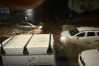 Nighttime flooded street in Briton Ferry with several vehicles driving through high water.