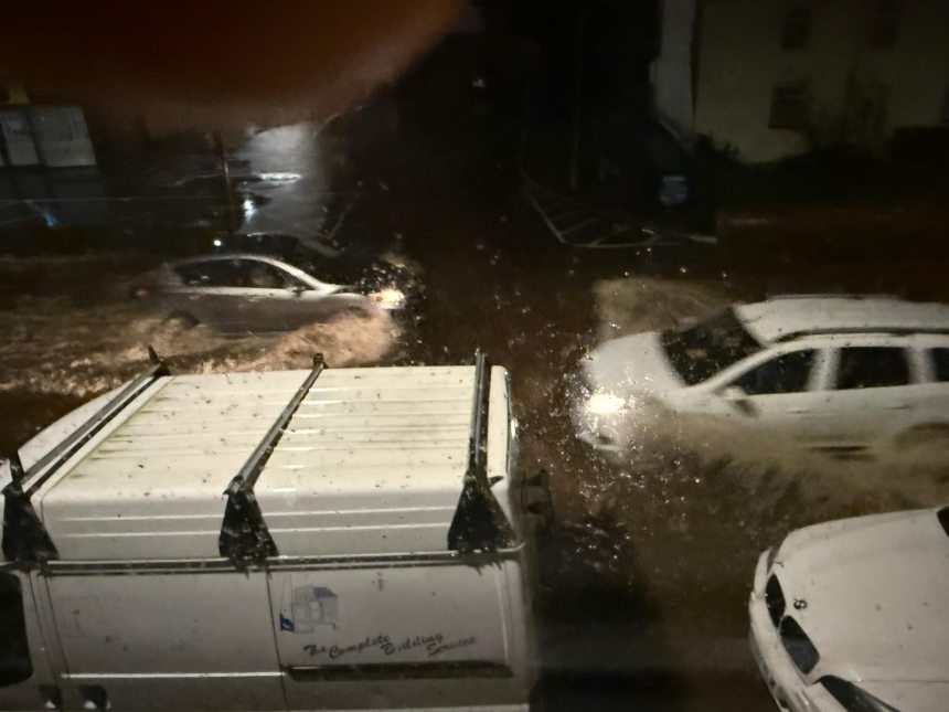 Nighttime flooded street in Briton Ferry with several vehicles driving through high water.