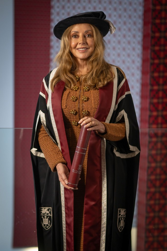 Carol Vorderman in academic regalia holding Swansea University diploma scroll during honorary degree presentation.