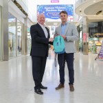 Julian John and Adam Gibbons shake hands inside Swansea’s Quadrant Shopping Centre, holding a sensory pack.